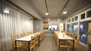 A conference room with long tables and wooden chairs, a television screen, and a window with stickers. - Bluefish Guesthouse - Hostel (Busan)