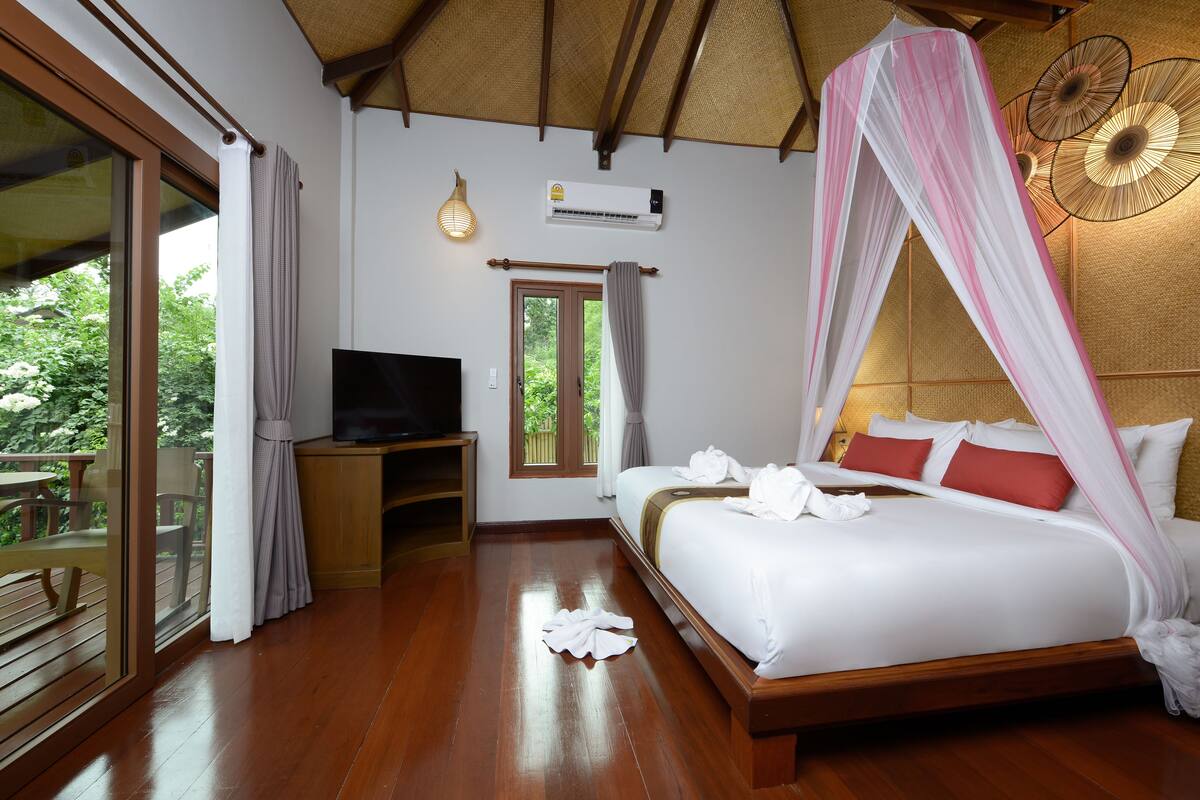 Een slaapkamer met een bed, een televisie en een raam met uitzicht op groen.