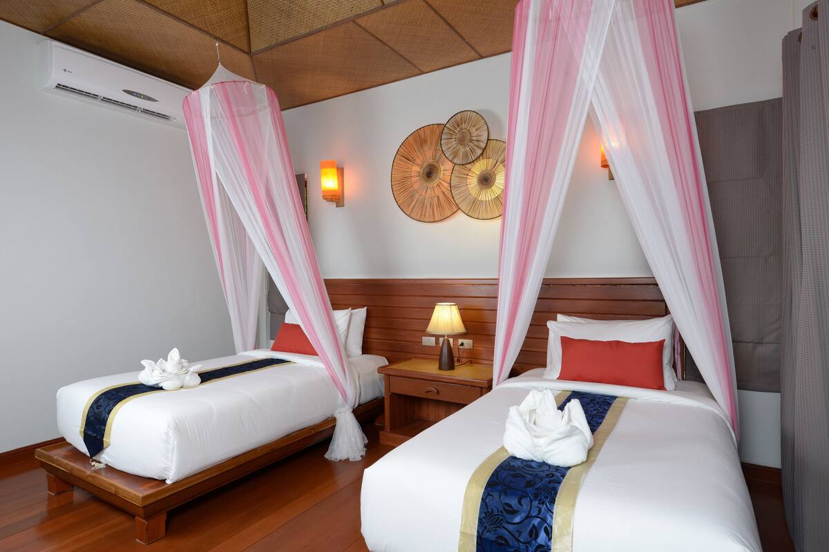 Een hotelkamer met twee bedden, elk voorzien van een hemelbed, een nachtkastje met een lamp en een decoratief object aan de muur.