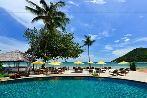 A poolside area with lounge chairs and umbrellas, a thatched-roof structure, and a view of the sea. - PingChan Koh Phangan Beachfront Resort (Ko Pha-ngan)