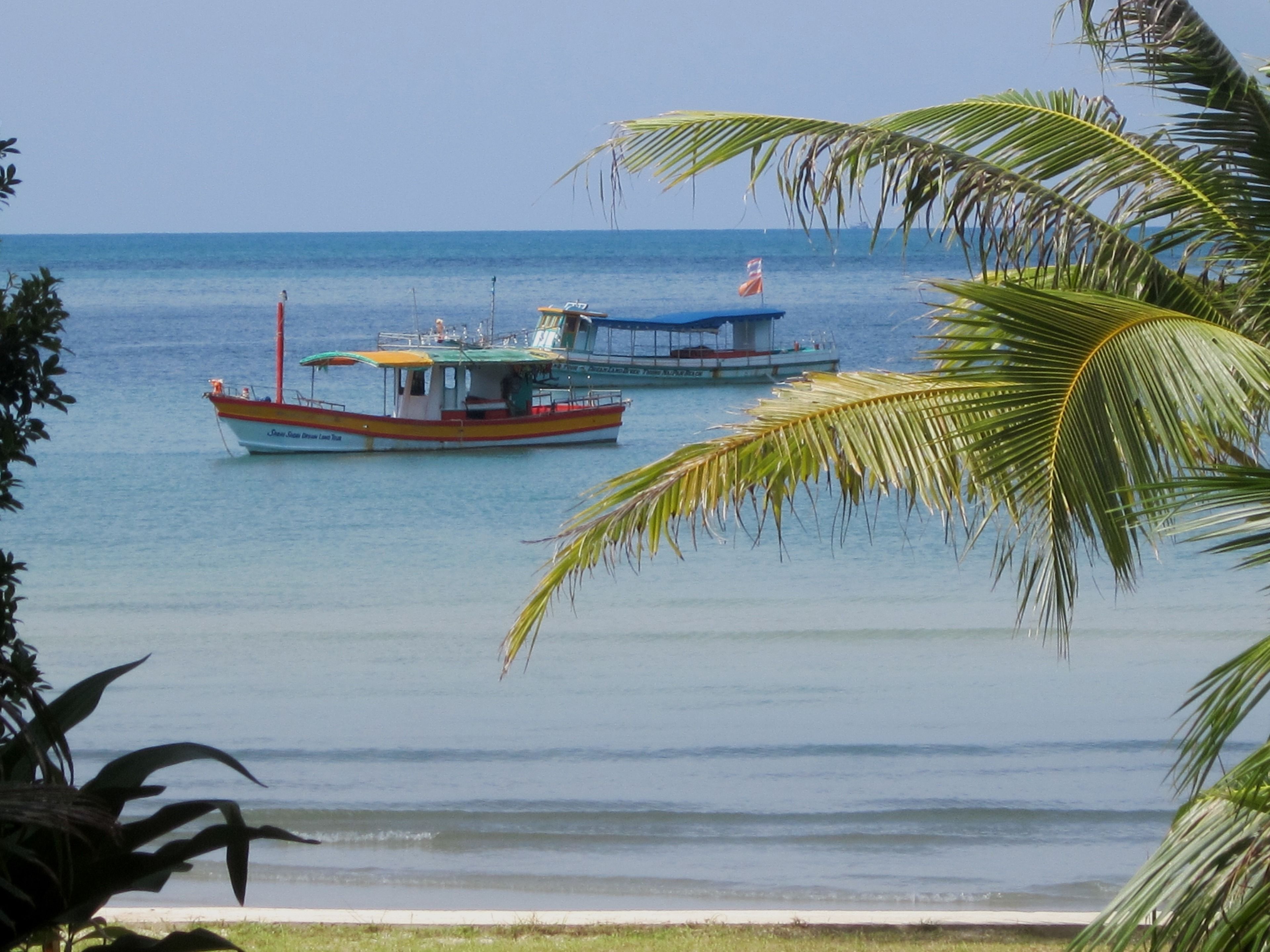 A calm sea with two boats, one red and one blue, and a small island with a flag in the distance.