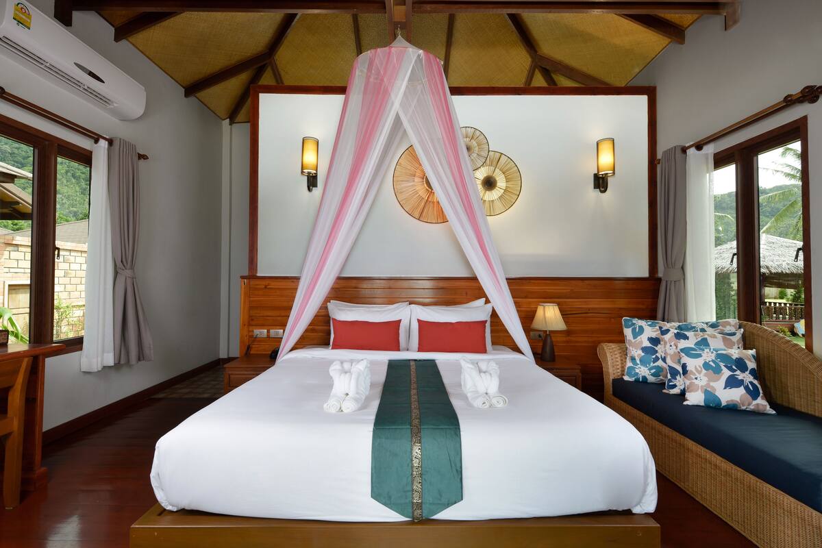 Een hotelkamer met een bed, een nachtkastje, een bank en uitzicht op het landschap.