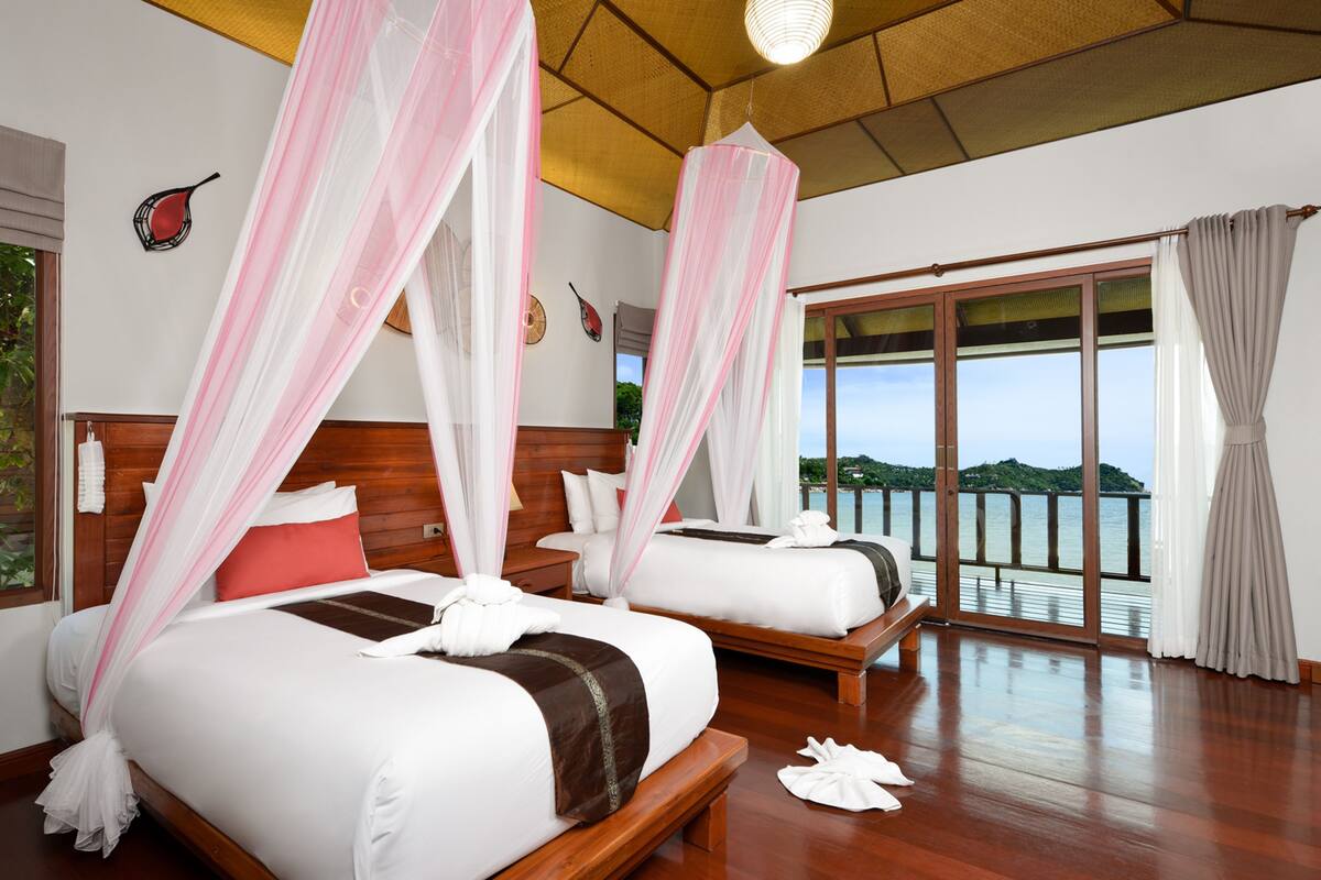 Een hotelkamer met twee bedden, een groot raam met uitzicht op zee en een houten plafond.
