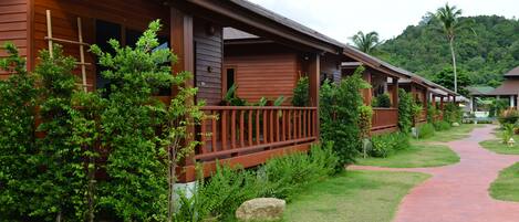 Una hilera de cabañas de madera con balcones, rodeadas de abundante vegetación y un sendero pavimentado.