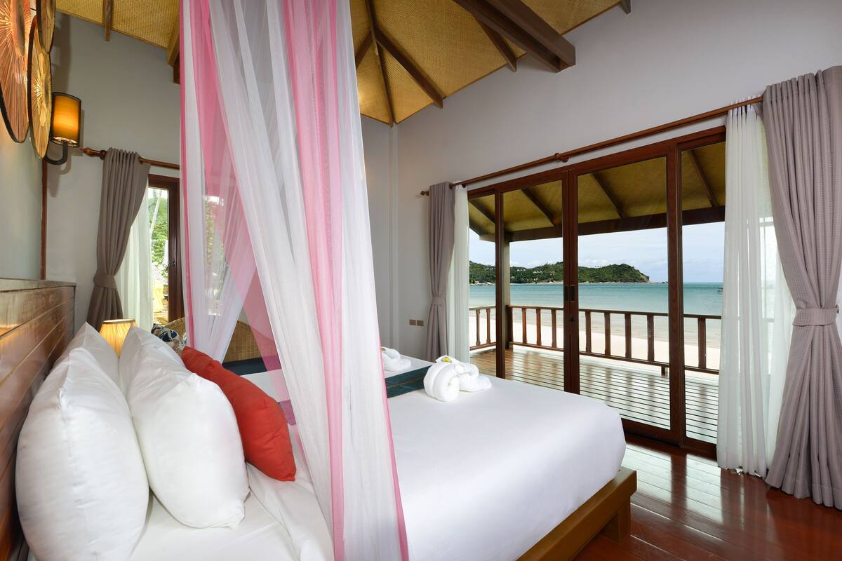 Een slaapkamer met een groot bed, een hemelbed en uitzicht op het strand.