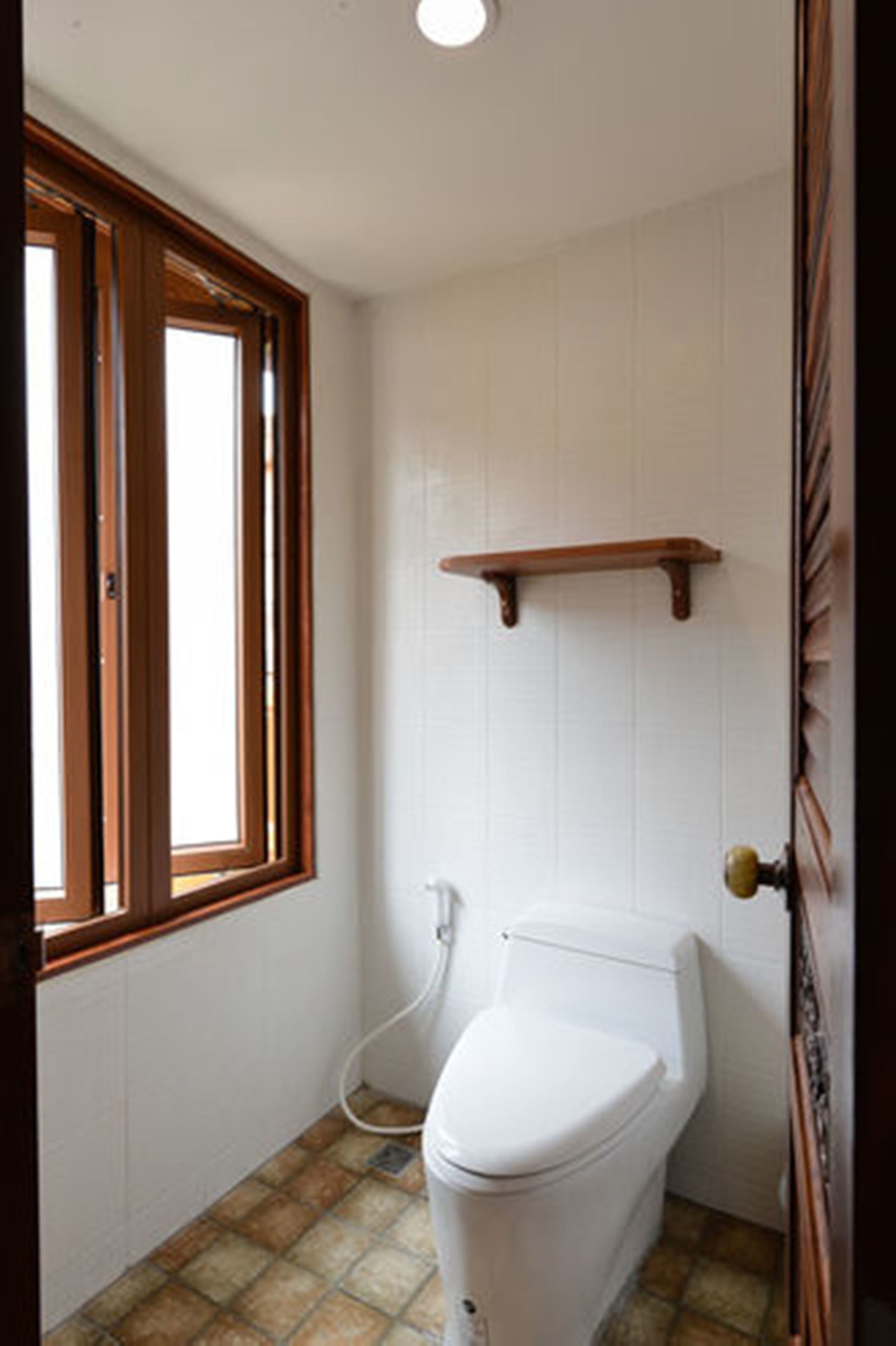 Un baño con inodoro, ventana y estante de madera.