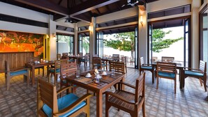 Un restaurant avec des tables et des chaises en bois, de grandes fenêtres et un ventilateur de plafond.