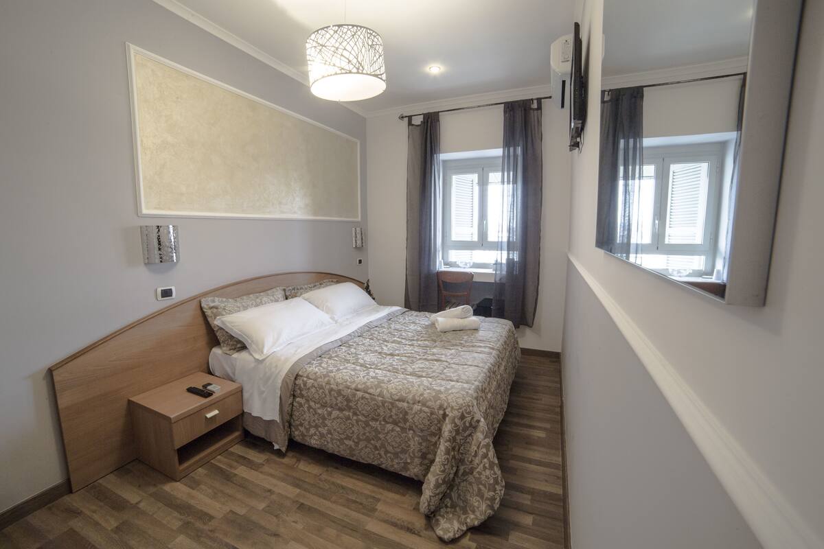 A bedroom with a wooden bed, bedside table, and a large window with curtains.