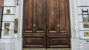 Une grande porte en bois richement décorée, ornée d’une poignée de porte en laiton, flanquée de colonnes blanches et surmontée d’une arche décorative.