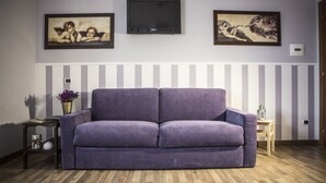 Un salon avec un canapé violet, un téléviseur à écran plat et deux œuvres d’art encadrées accrochées au mur.