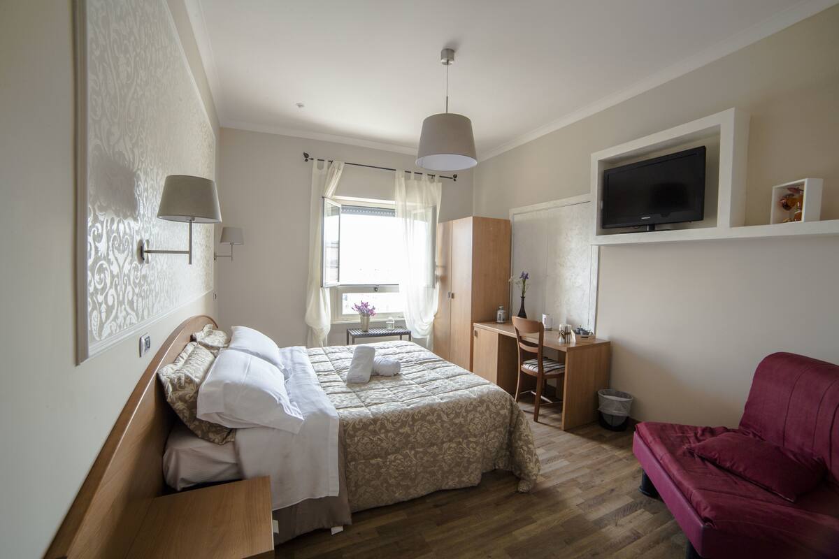 A bedroom with a bed, a desk, a chair, a TV, and a red sofa.