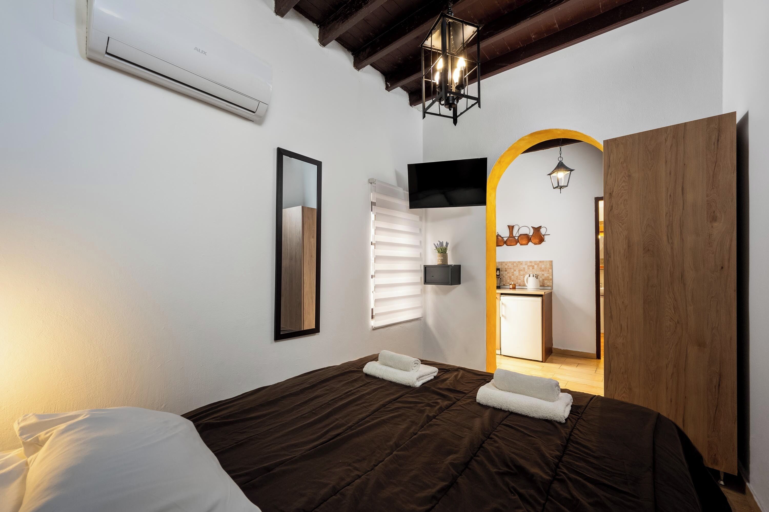 A bedroom with a large bed, a bedside table, a mirror, and a wooden wardrobe.