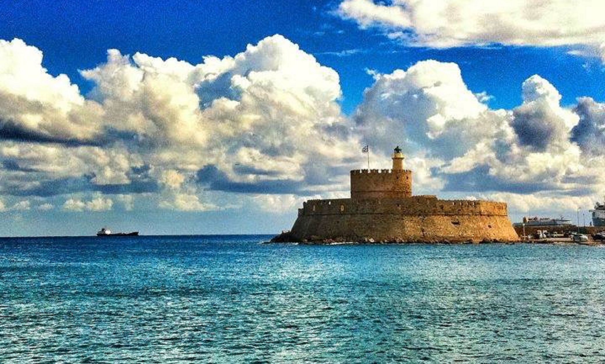 Une fortification côtière dotée d’un phare, entourée d’une mer calme et d’un ciel partiellement nuageux.
