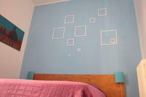 A bedroom with a blue wall, a wooden headboard, a pink bedspread, and a painting of a building. - Scipione B&B (Rome)