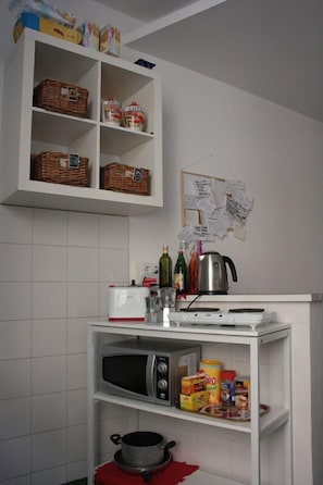 A kitchen with white cabinets, a microwave, a toaster, and various food items. - Scipione B&B (Rome)