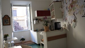 A small kitchen with a window, a refrigerator, a coffee maker, and a cluttered wall with notes. - Scipione B&B (Rome)