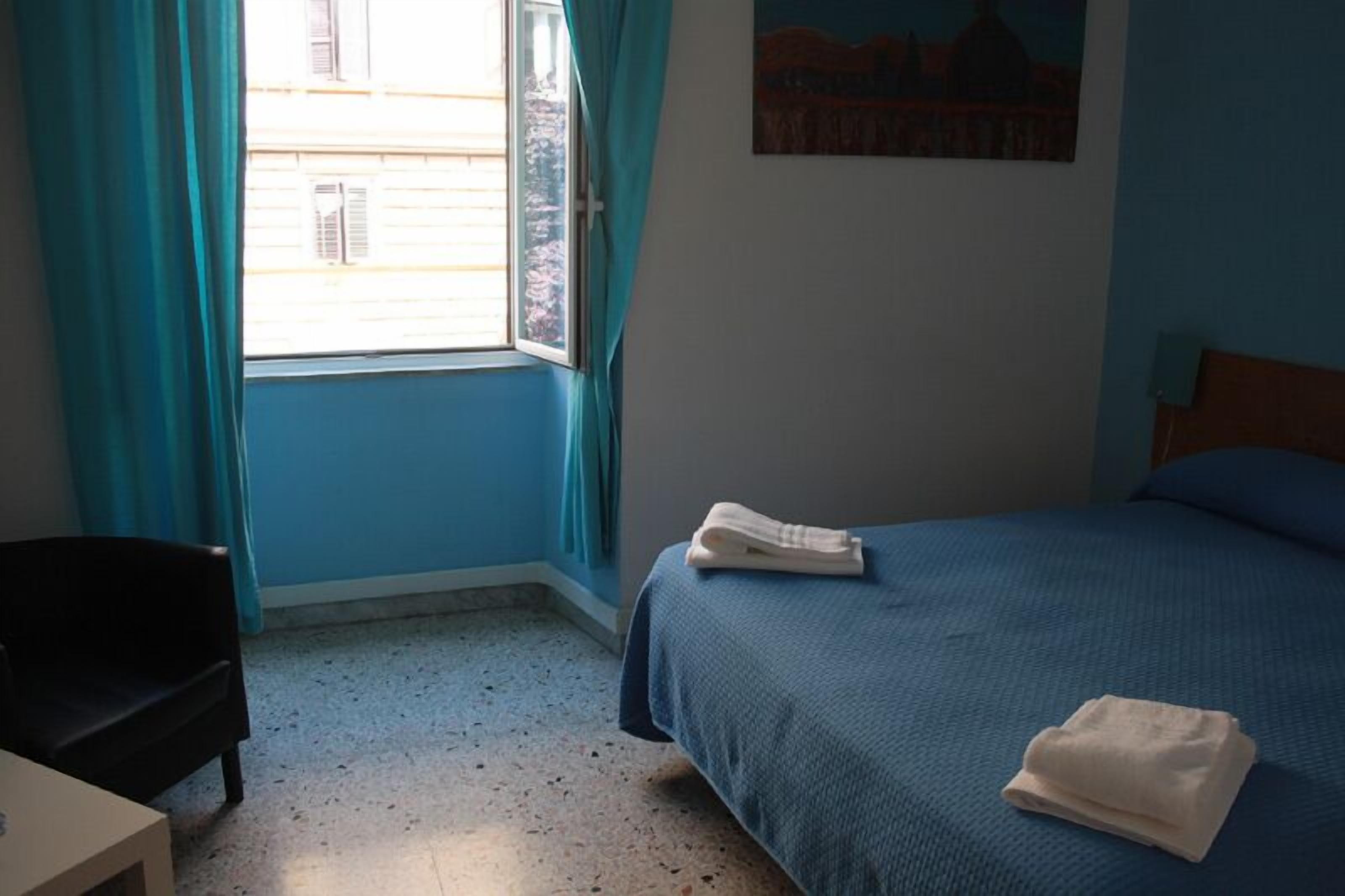 A bedroom with a bed, a chair, a window with curtains, and a painting on the wall.