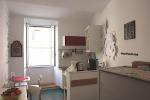 A compact kitchen with a window, white cabinets, a coffee machine, and a fruit basket. - Scipione B&B (Rome)