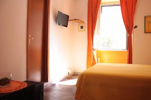 A hotel room with a bed, a television mounted on the wall, and a window with orange curtains.