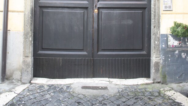 A large, dark wooden double door with two metal knockers, set in a stone frame. - Scipione B&B (Rome)