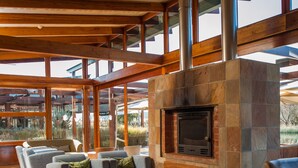 A spacious living area with a stone fireplace, wooden beams, and large windows. - Forum Homini Boutique Hotel (Krugersdorp)