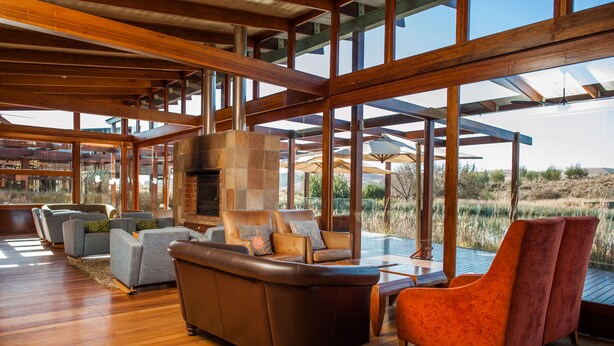 A spacious living area with wooden flooring, a fireplace, and large windows offering a view of the outdoors. - Forum Homini Boutique Hotel (Krugersdorp)
