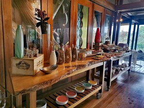A buffet setup with various dishes and condiments, wooden furniture, and a view of the outdoors. - Forum Homini Boutique Hotel (Krugersdorp)