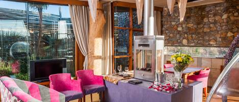 A modern living room with a stone wall, a fireplace, and a large window overlooking a garden.