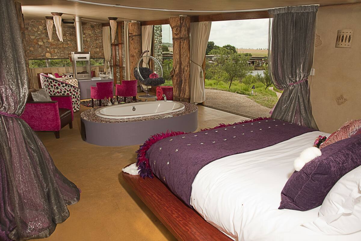 Un dormitorio con una cama grande, un jacuzzi circular y una zona de estar con un espejo y sillones.
