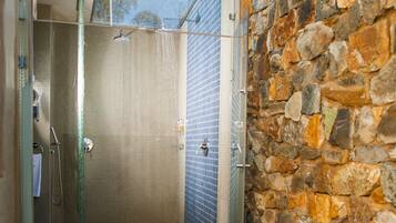 Shower area features a glass enclosure and natural stone wall, with a pebble-covered floor and stepping stones leading in.