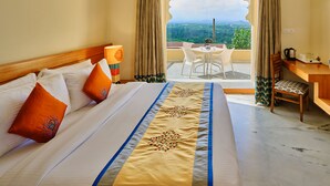 A hotel room with a large bed, a dining area with a table and chairs, and a view of the landscape through a window with curtains.