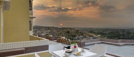 A terrace with a table set for dining, overlooking a scenic landscape with hills and a sunset.