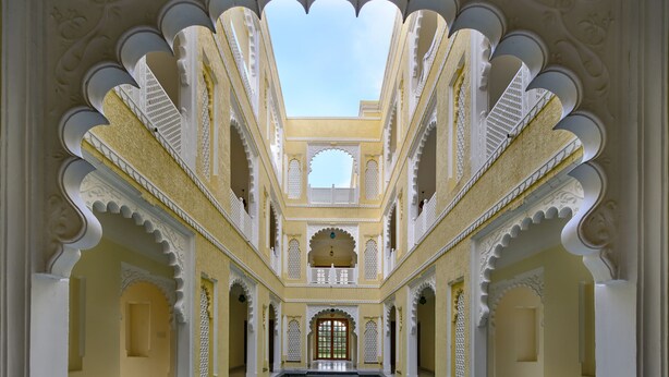A corridor with a central pool, ornate white arches, and a high ceiling.