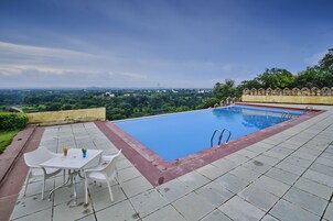 Una piscina con vistas al paisaje, una mesa con sillas y una mesita con un florero y una planta.