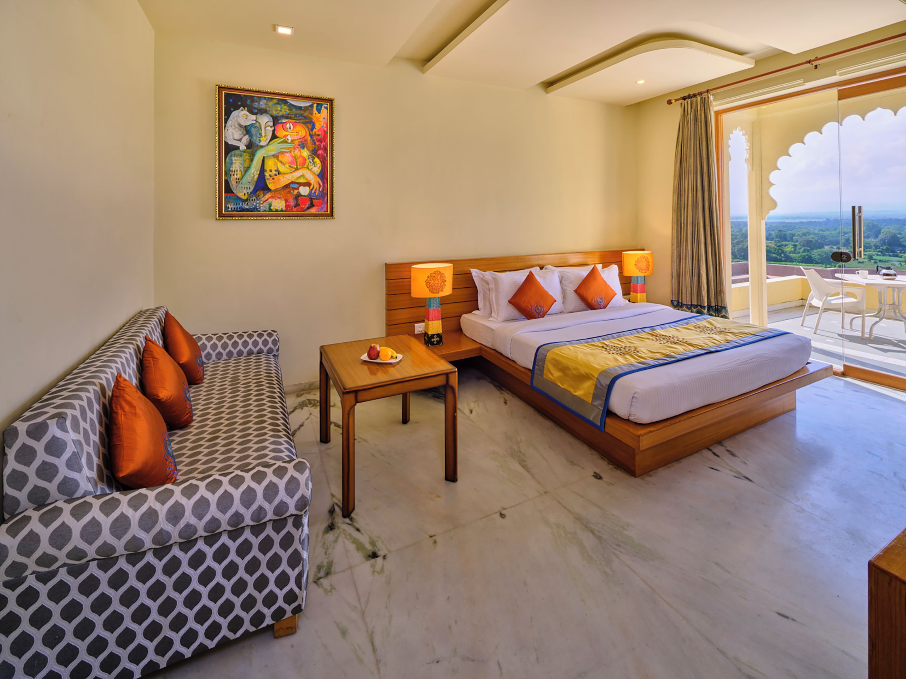 Habitación de hotel con cama, sofá, una mesita con fruta y un cuadro en la pared.
