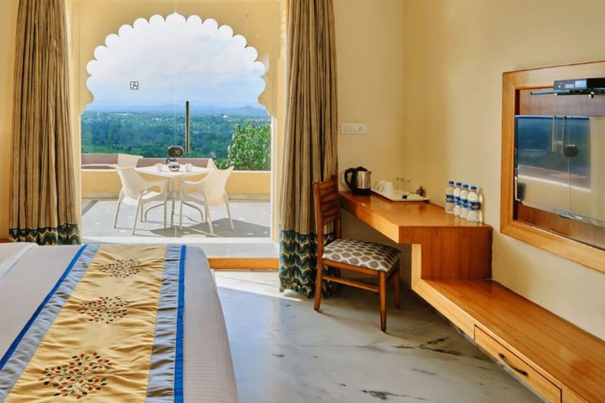 A hotel room with a bed, a desk, a chair, a table, and a view of the landscape.