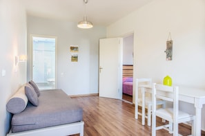 Quarto com cama, mesa de cabeceira e uma cadeira. Há uma porta que dá para outro cômodo.