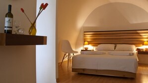 Un dormitorio con cabecera de madera, una mesita de noche con lámpara, una silla y un estante con botellas de vino y flores.