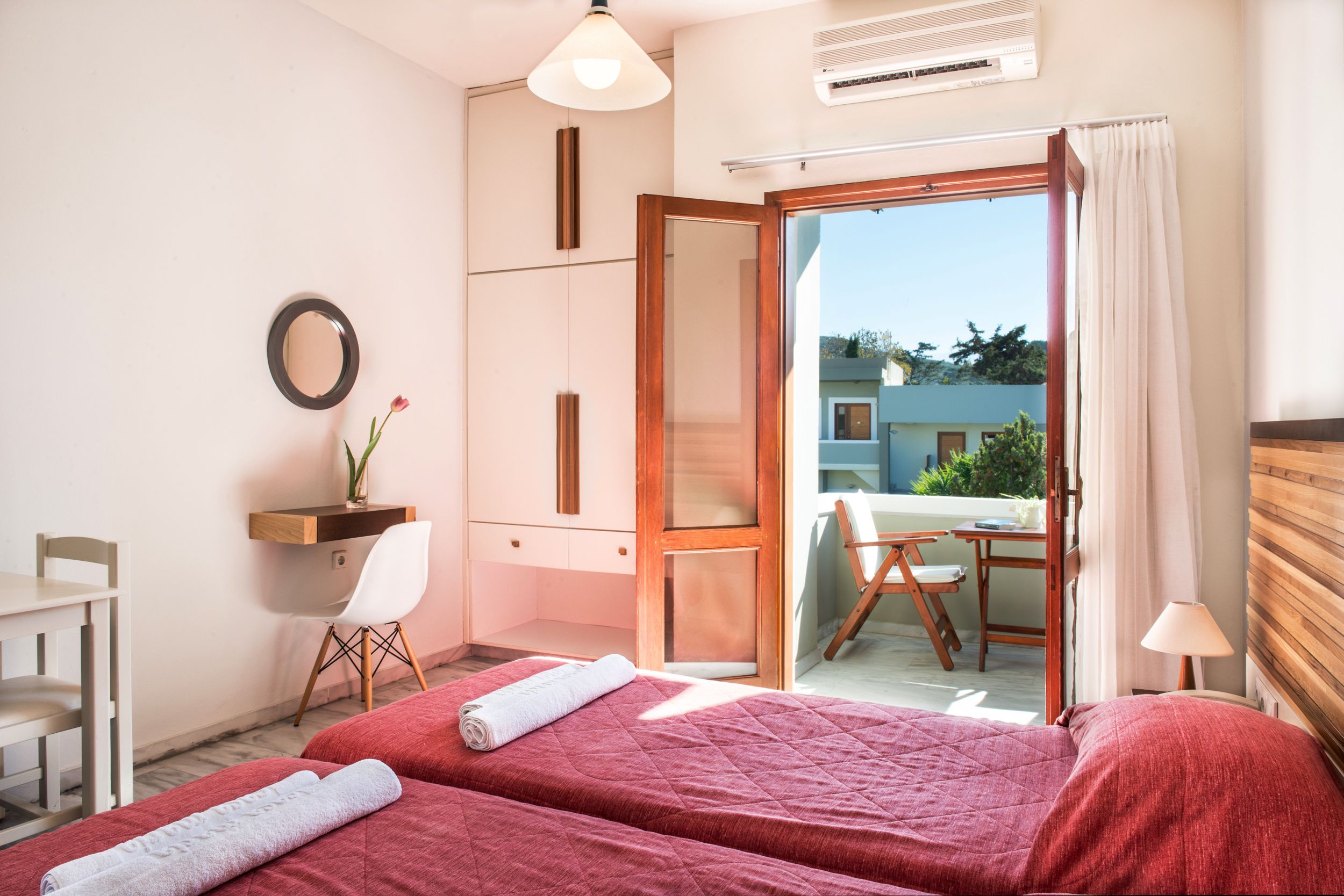 Quarto de hotel com duas camas, uma escrivaninha, uma cadeira, um espelho e vista para o exterior.