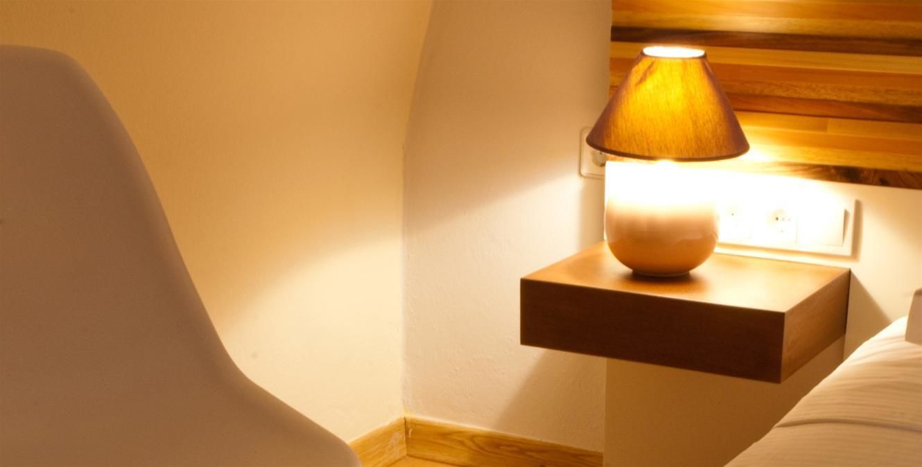 Una mesita de noche con una lámpara, una silla y una cama en una habitación de hotel.