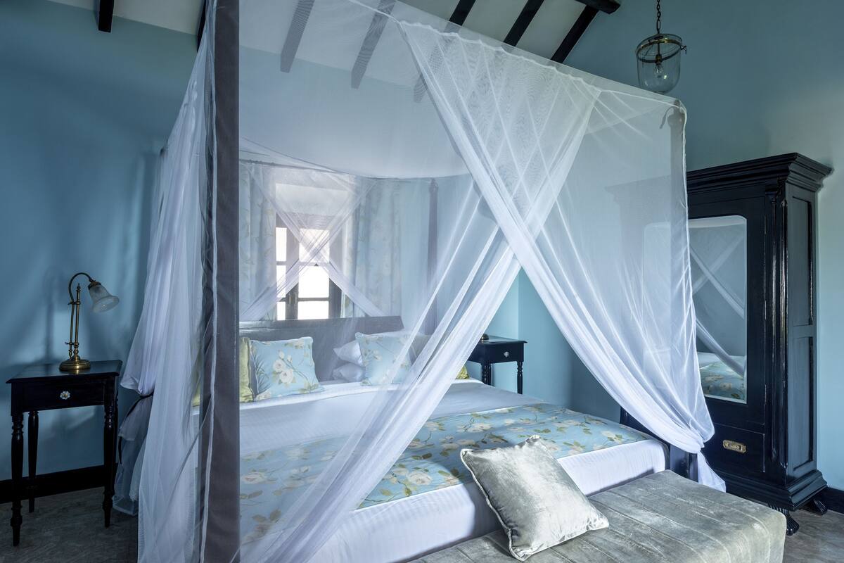 A bedroom with a four-poster bed, a nightstand, a lamp, and a wardrobe.