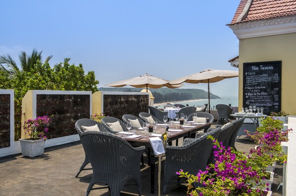 Un espace de restauration en plein air avec des chaises et des tables en osier, des parasols et un panneau affichant le menu.