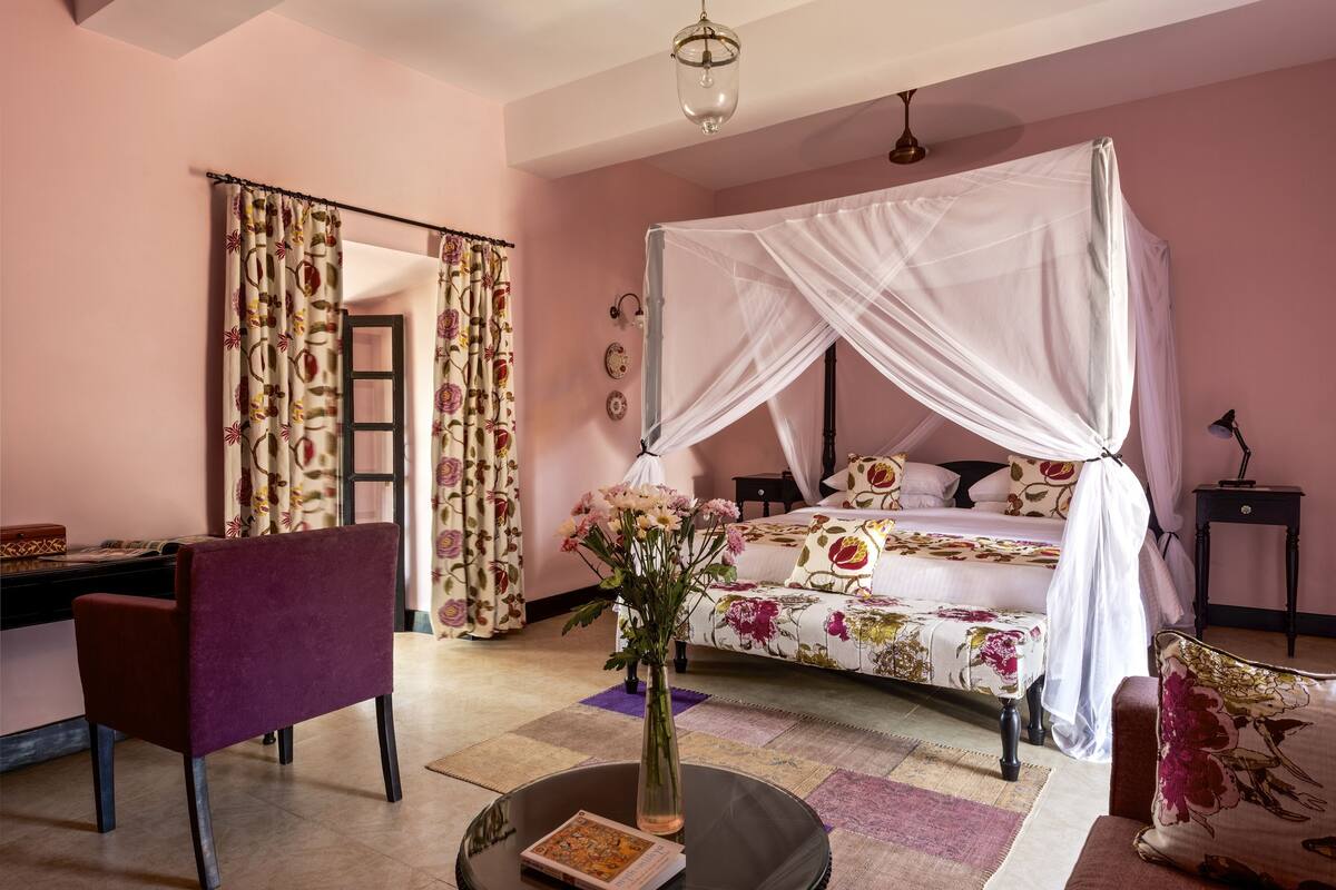 A bedroom with a four-poster bed, a desk, a chair, and a vase with flowers.