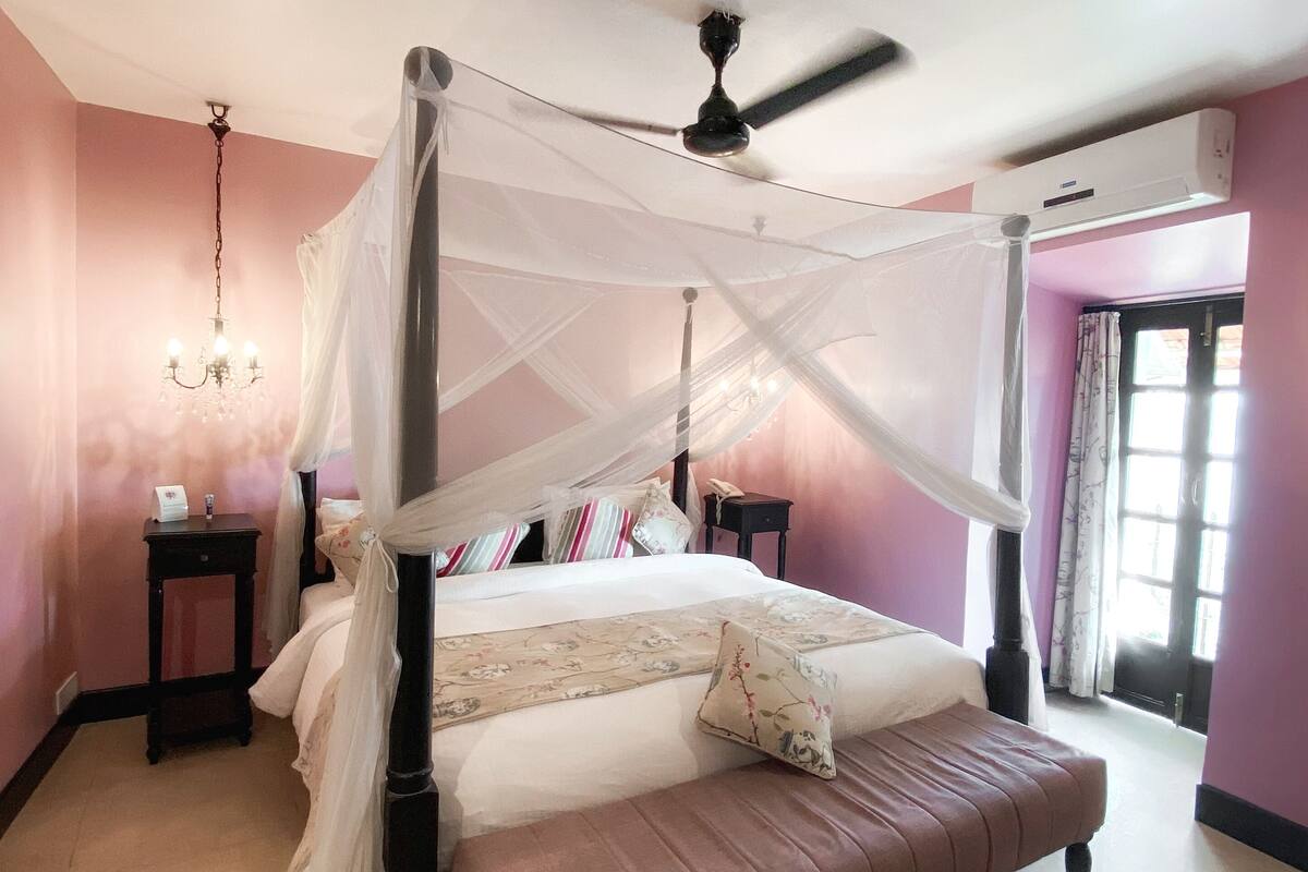 A bedroom with a four-poster bed, a ceiling fan, a bedside table, and a nightstand.