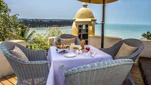 Une table à manger avec vue sur l’océan, des chaises en osier et une petite construction surmontée d’un toit en forme de dôme.