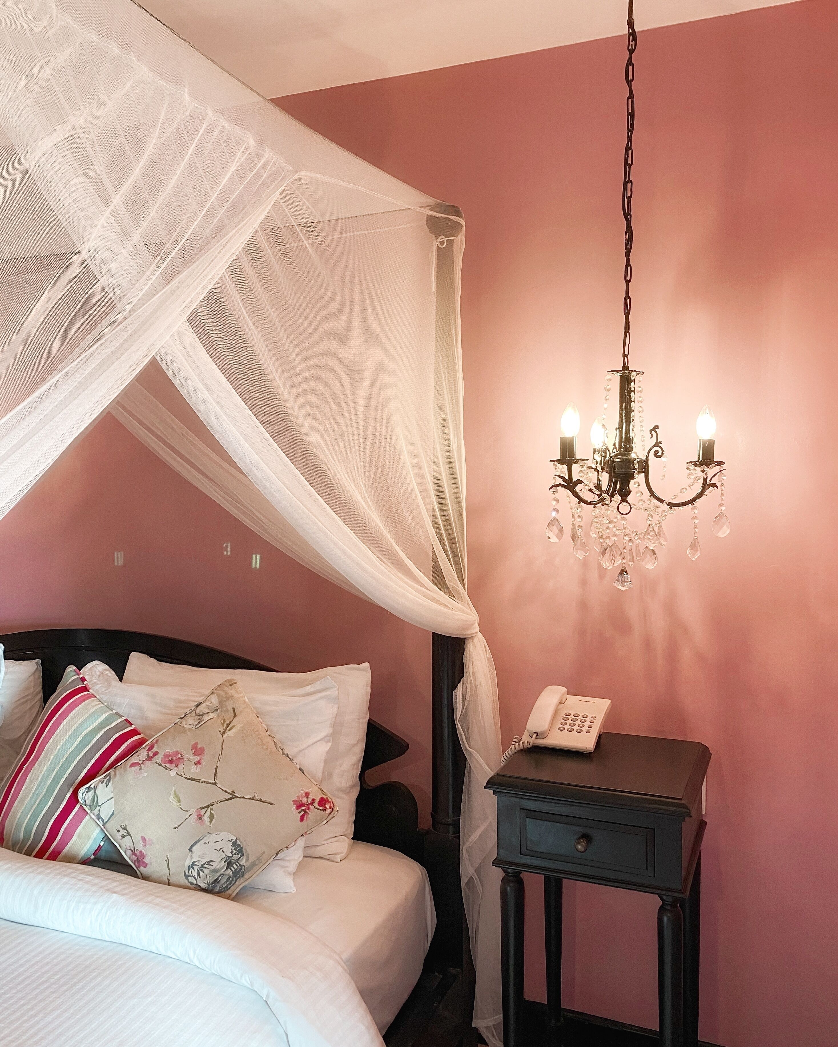 A bedroom with a bed, a bedside table with a phone, a chandelier, and a canopy bed.