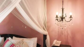 A bedroom with a bed, a bedside table with a phone, a chandelier, and a canopy bed.