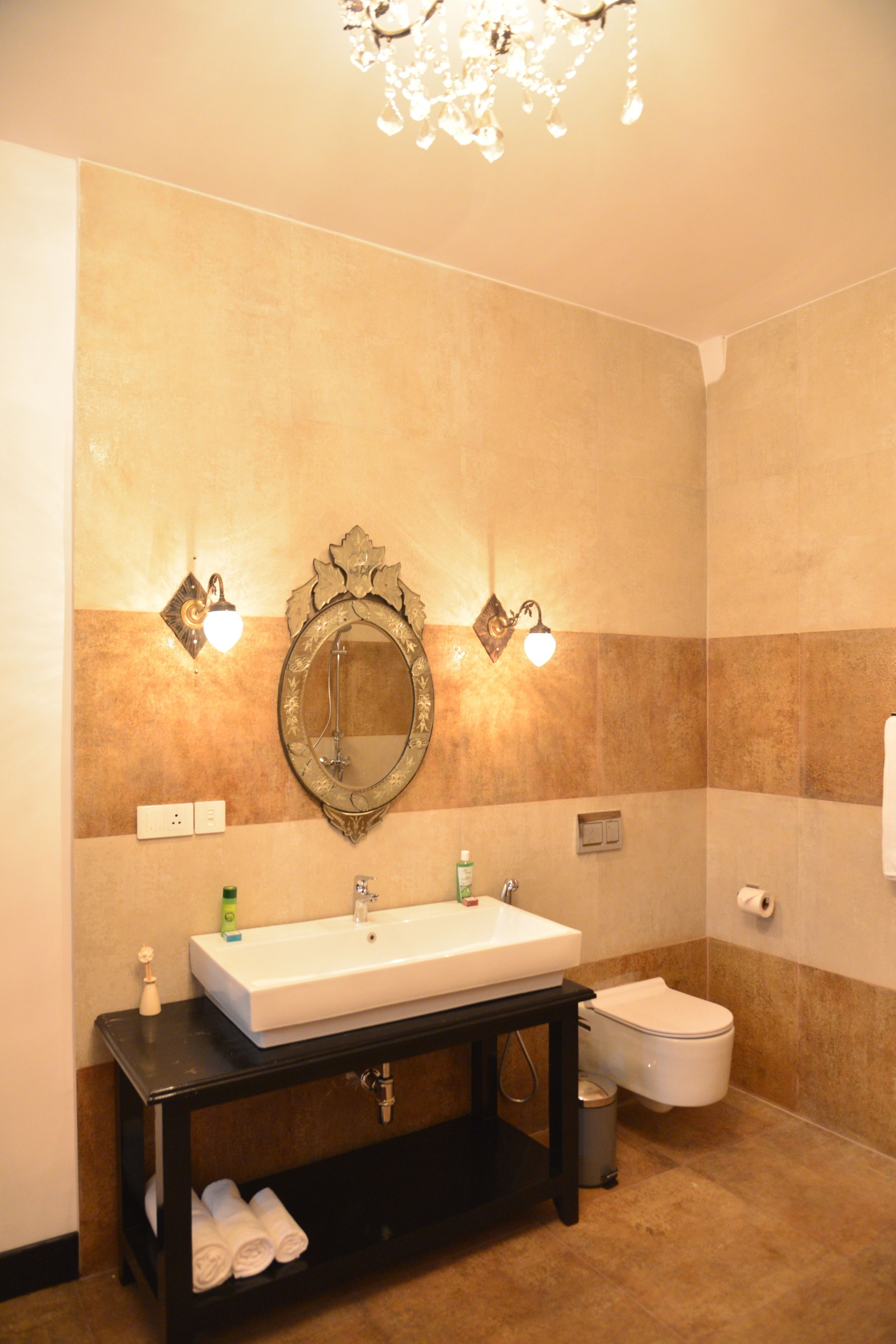 A bathroom with a white sink, a mirror, two wall-mounted lights, a toilet, and a trash can.