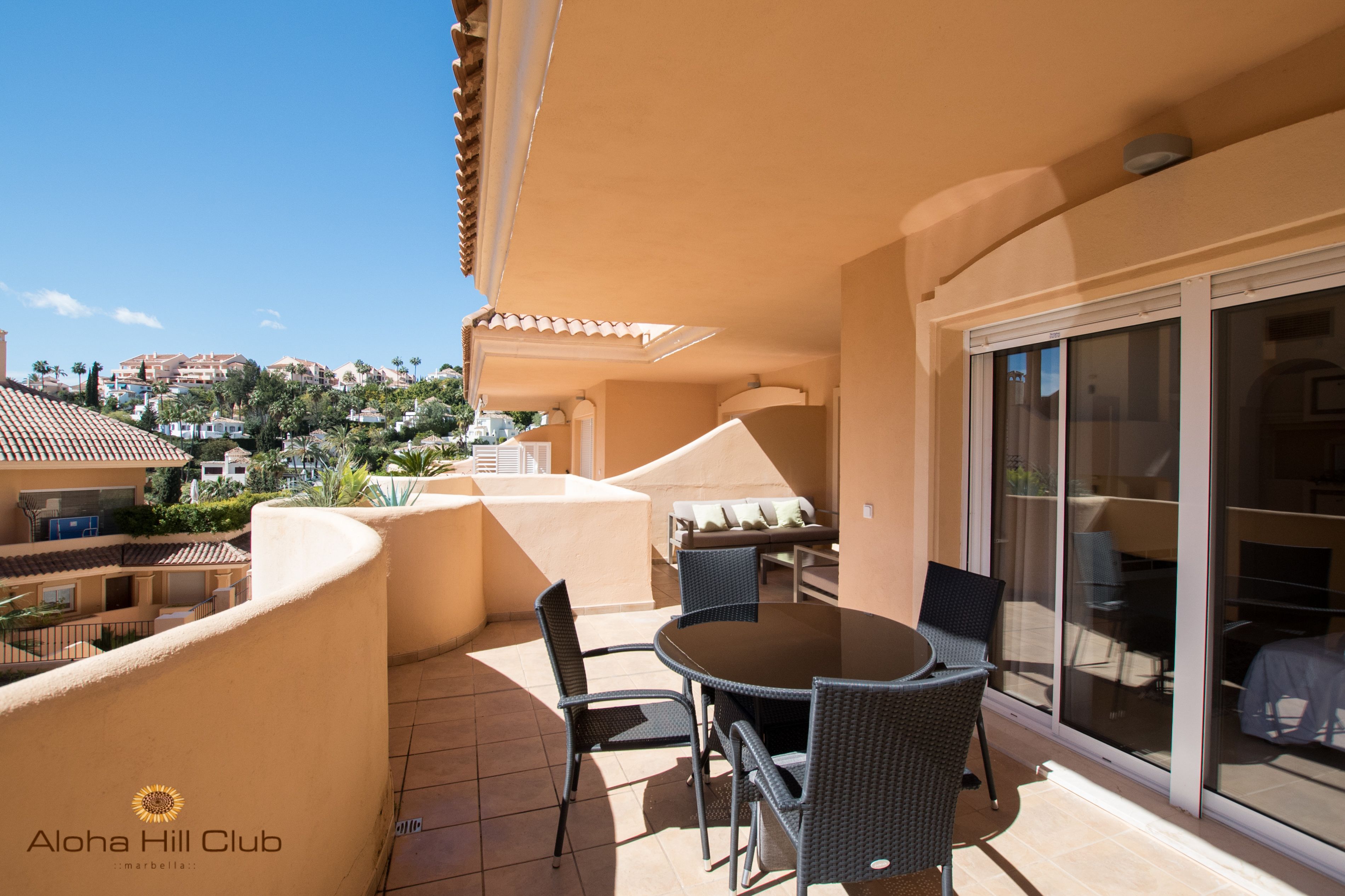 An outdoor patio with a round table and chairs, a sofa, and a sliding glass door leading to a balcony.