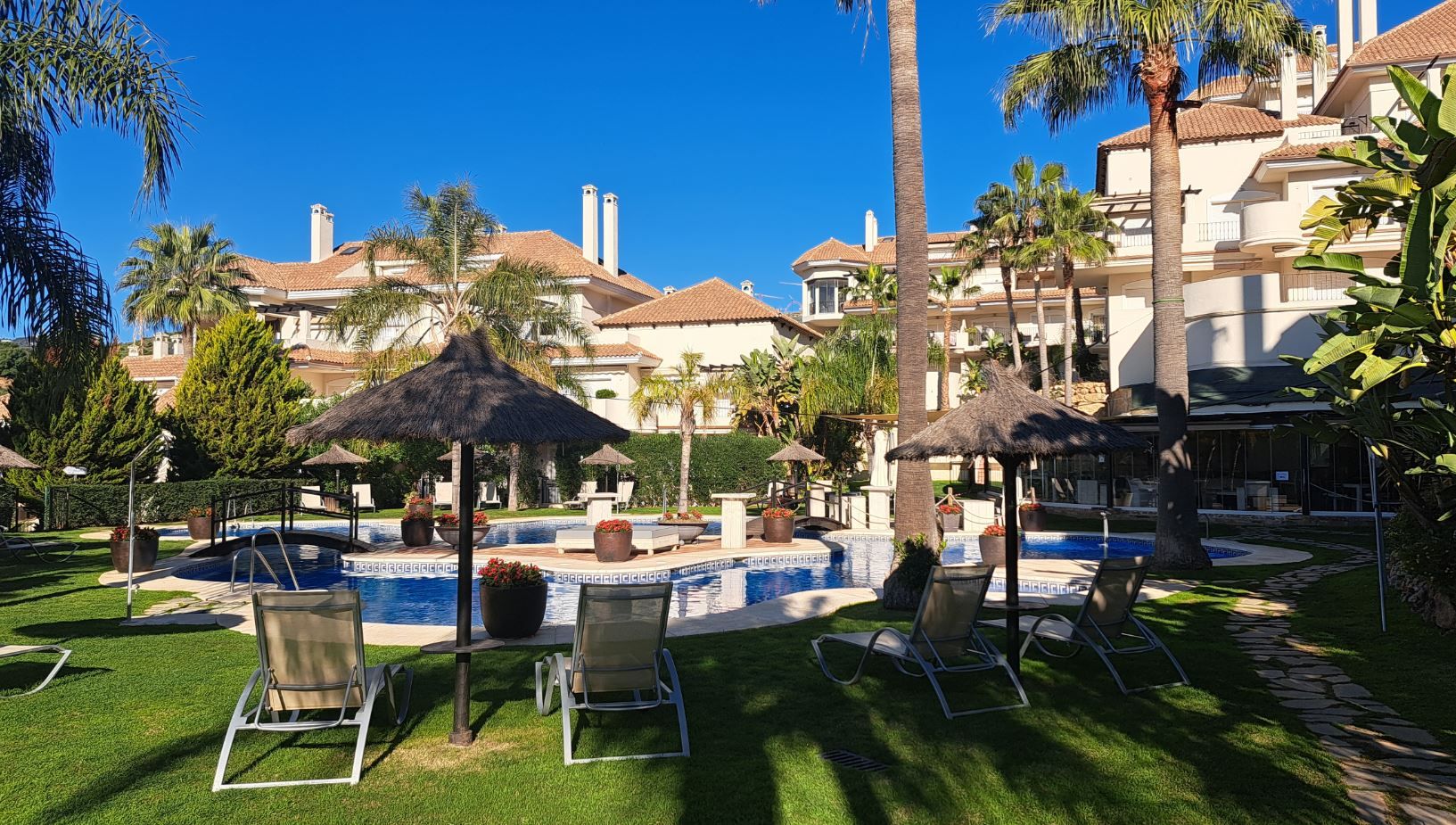 Ein Poolbereich eines Resorts mit Liegestühlen, Sonnenschirmen und blauem Himmel.